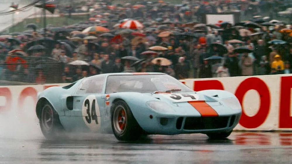 A dramatic, high-angled view of historic Le Mans race cars, showcasing the evolution of their sleek, aerodynamic designs over the decades. The foreground features a 1960s-era Porsche 917 with its distinctive long-tail body shape, gleaming under warm, directional lighting. In the middle ground, a 1980s Jaguar XJR-9 LM cuts through the frame, its sharply-swept fenders and curvaceous silhouette hinting at the increasing emphasis on downforce and efficiency. The background is filled with a blurred progression of other iconic Le Mans competitors, ranging from early 20th century racers to cutting-edge modern prototypes, representing the race's enduring legacy of technological innovation. The scene conveys a sense of speed, power, and the march of automotive progress through the lens of this legendary endurance competition.