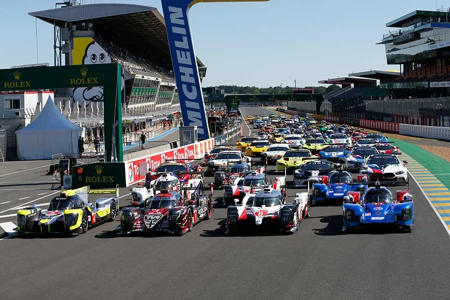A dramatic night scene of the historic 24 Hours of Le Mans endurance race. In the foreground, a fleet of sleek, high-performance racing cars speed through the darkness, their headlights cutting through the shadows. The middle ground features the famous pit crews hustling to service the vehicles, their movements illuminated by the glow of floodlights. In the background, the iconic silhouette of the Le Mans circuit is visible, with its long straightaways and tight turns. The atmosphere is one of intense competition, with a sense of history and tradition permeating the scene. The lighting is dramatic, with deep shadows and high contrast, creating a moody and evocative aesthetic.